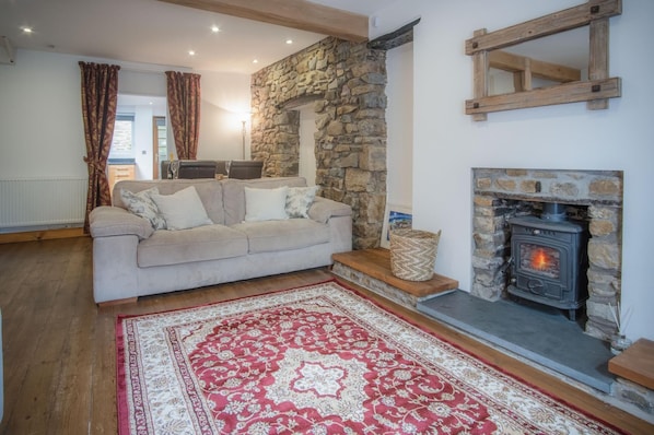 Una sala de estar acogedora con chimenea de piedra, un sofá y un tapete rojo estampado.