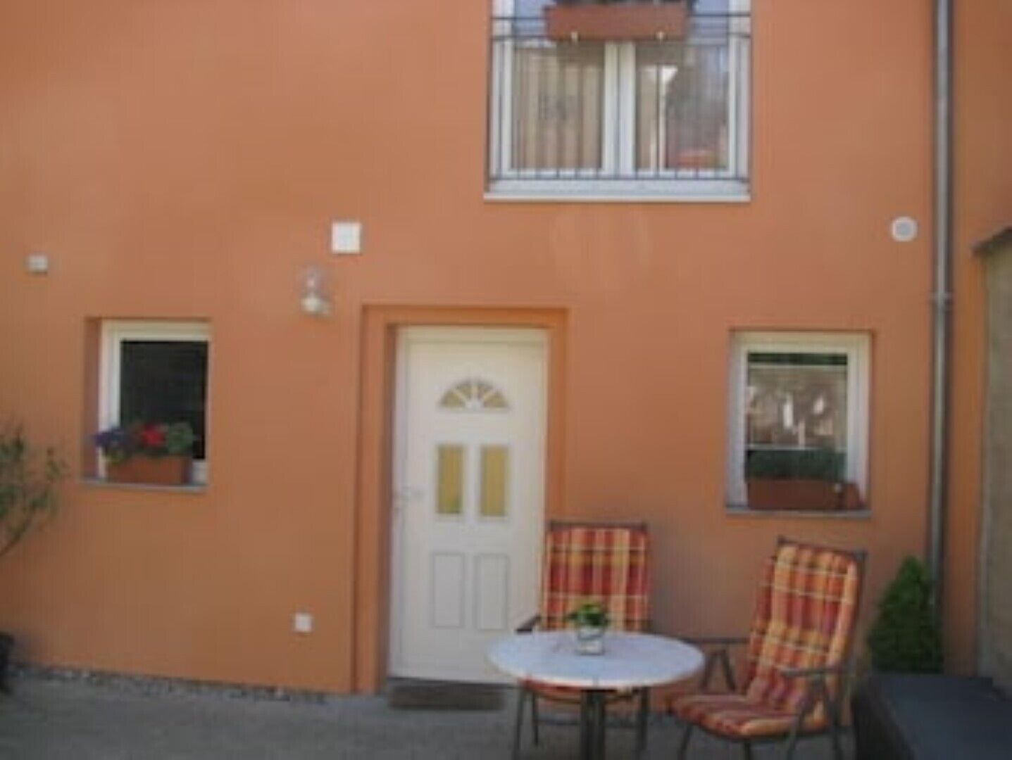 A building with a single door, two windows, and a small table with chairs.