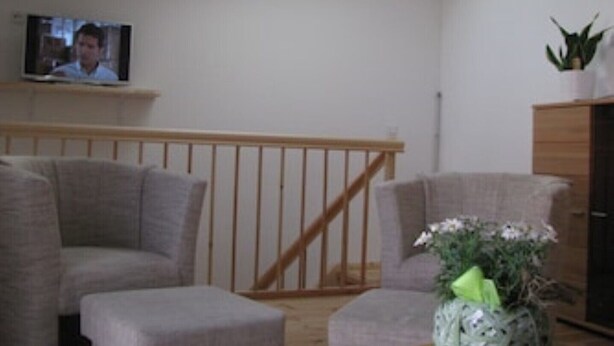 Un salon avec un téléviseur fixé au mur, une rambarde en bois et une plante en pot posée sur un meuble.