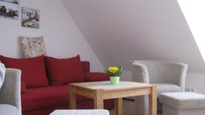 Un salon moderne avec un canapé rouge, un fauteuil gris, une petite table en bois et un pouf gris.