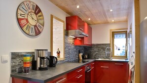 Una cocina moderna con gabinetes rojos, un reloj de pared grande y un salpicadero de piedra.