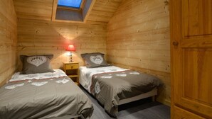 Una habitación de cabaña acogedora con dos camas, un tragaluz y una mesita de noche con lámpara.