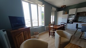 Moderni olohuone, jossa on televisio, kaksi nojatuolia, ruokapöytä sekä keittiöalue, jossa on mikroaaltouuni ja uuni.