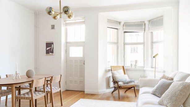 A bright, open living space with a wooden dining table, chairs, a sofa, and a large window providing natural light. - 1br apartment with balcony and sea view (Helsinki)