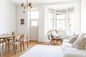 A bright, open living space with a wooden dining table, chairs, a sofa, and a large window providing natural light. - 1br apartment with balcony and sea view (Helsinki)
