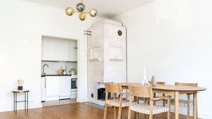 A modern kitchen with white cabinets, a dining area with a wooden table and chairs, and a white fireplace. - 1br apartment with balcony and sea view (Helsinki)