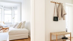 A modern living room with a white sofa, a wooden bench, and a coat rack with a bag and jacket. - 1br apartment with balcony and sea view (Helsinki)