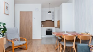 A modern kitchen with white cabinets, a wooden door, and a dining area with a table and chairs. - WestSide Apartments by FirstHost (Budapest)
