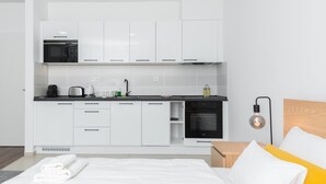 A modern hotel room with a kitchenette, a bed with white and yellow bedding, and a nightstand with a lamp. - WestSide Apartments by FirstHost (Budapest)