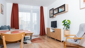 A modern living room with a wooden dining table, chairs, a TV, a sofa, a rocking chair, and a potted plant. - WestSide Apartments by FirstHost (Budapest)