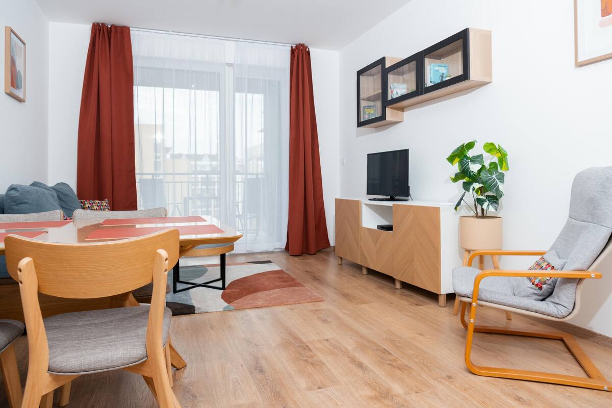 En moderne stue med et træspisebord, stole, et fjernsyn, en sofa, en lænestol og en potteplante.