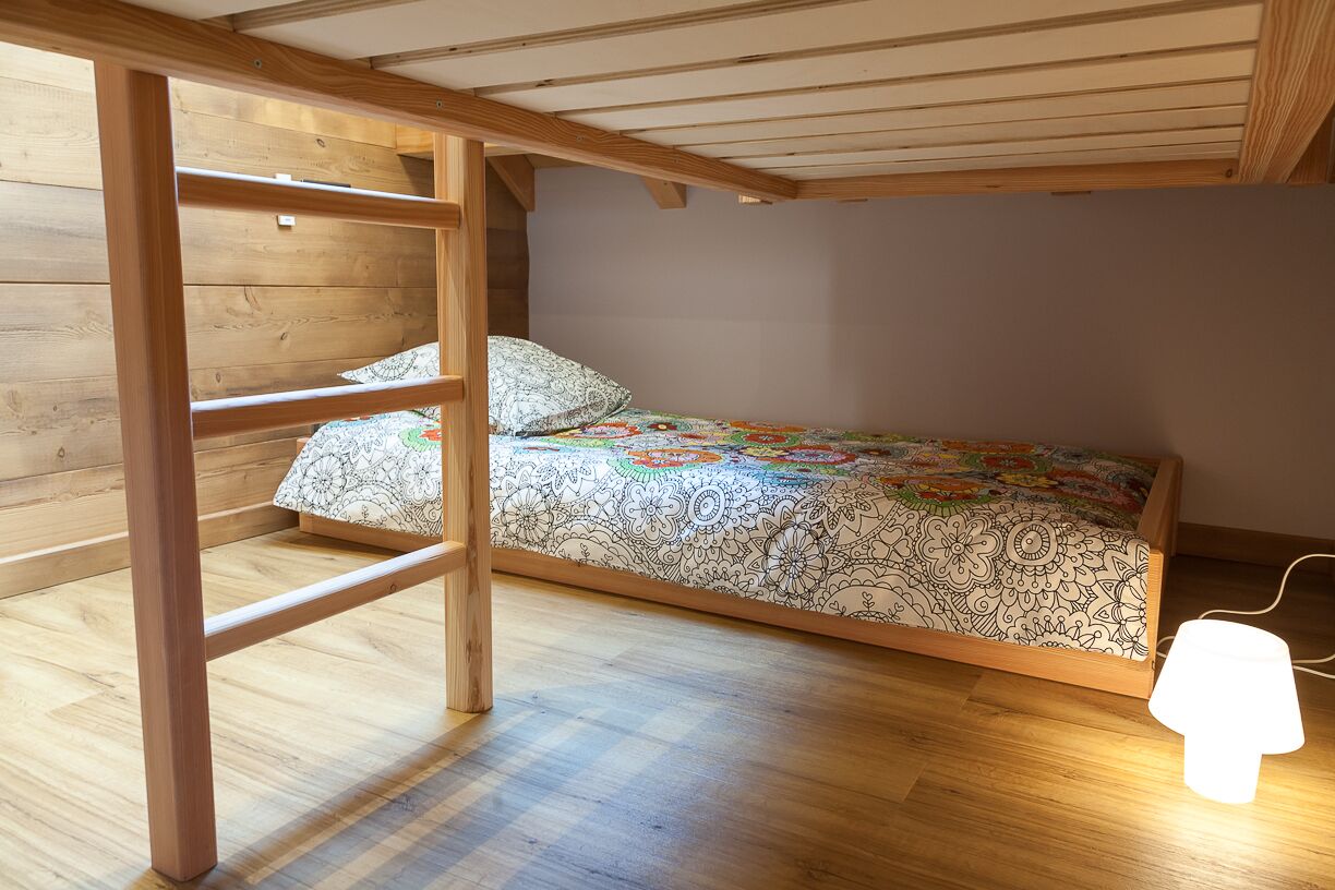 A bunk bed with a patterned bedspread, a wooden ladder, and a bedside table with a lamp.