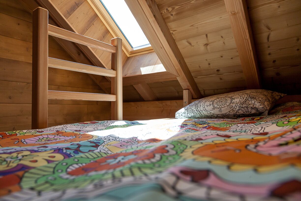 Une chambre à coucher aménagée dans les combles, avec un plafond vitré, une couvre-lit aux couleurs vives et un coussin à motifs.