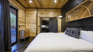 A wooden cabin bedroom with a large bed, a wooden ceiling, and a view through an open door.