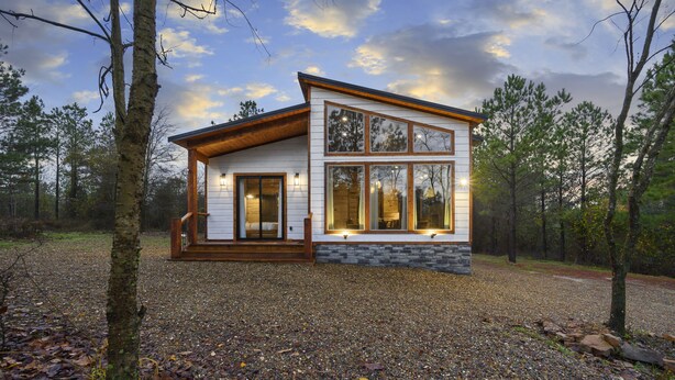 A modern cabin with a stone foundation, large windows, and a wooden deck.