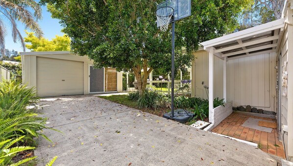 A residential garage with a covered driveway, a tree, and a small garden area.