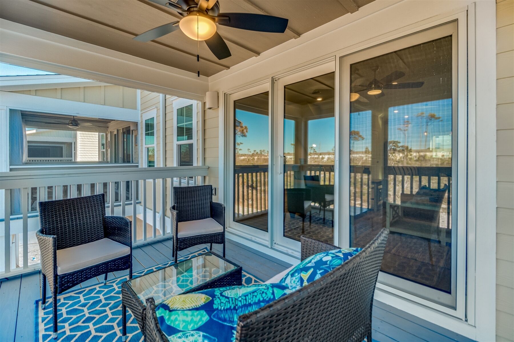 A covered outdoor deck with wicker furniture and a glass table, overlooking a residential area.