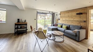 Un soggiorno moderno con un divano grigio, pavimento in legno e un'ampia porta-finestra scorrevole che si apre su un giardino.