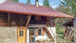 Un rustico chalet in legno con fondamenta in pietra, un balcone con ringhiera e una scala in legno che conduce all'ingresso.