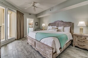 A bedroom with a large bed, a ceiling fan, a nightstand with a lamp, and a view through a sliding door.