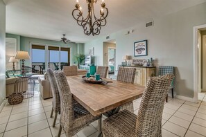 A spacious dining area with a wooden table surrounded by wicker chairs, a chandelier, and a view of the outdoors.