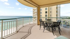 Een balkon met een tafel en stoelen, met uitzicht op een strand en de oceaan.