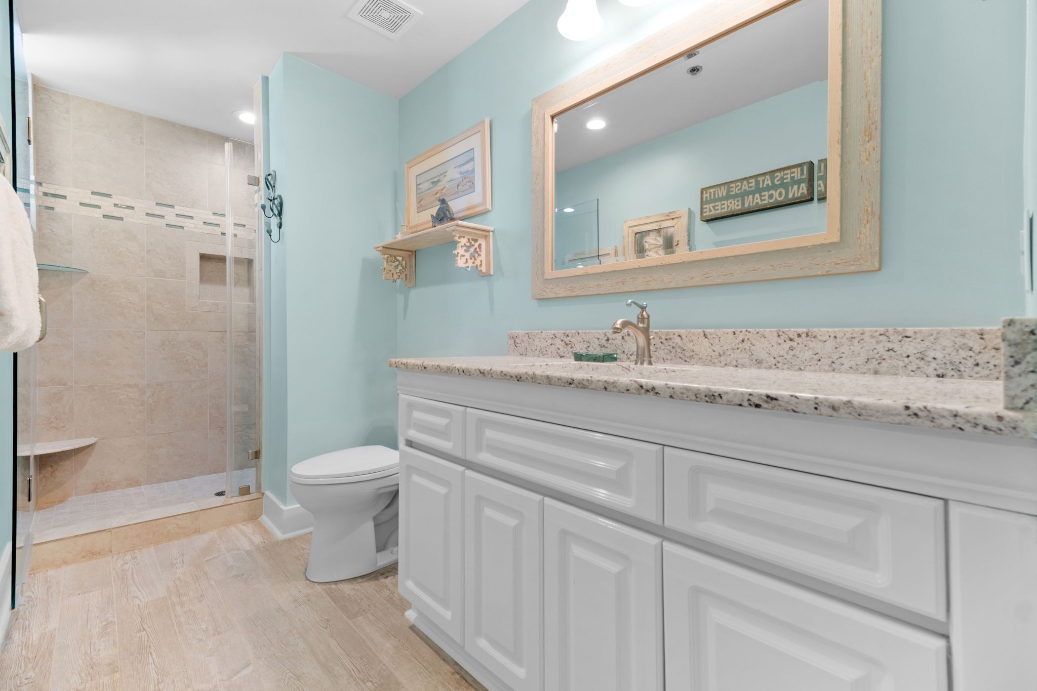 A bathroom with a shower, toilet, vanity with a mirror, and a framed picture on the wall.