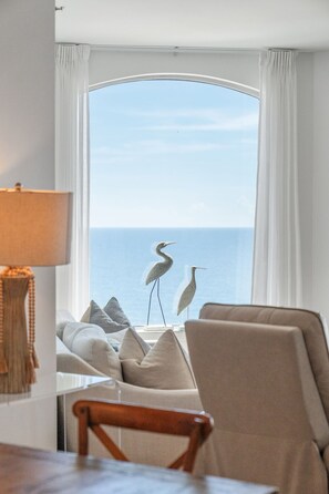 A room with a view of the ocean, a sofa, a chair, and two decorative bird sculptures. - Beach Colony Tower 14B - Indoor Pool - HASSLE-FREE CHECK OUT (Perdido Key)