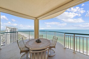 A balcony with a round table and chairs, overlooking a beach and ocean. - Beach Colony Tower 15B - Indoor Pool - HASSLE-FREE CHECK OUT (Perdido Key)