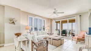 A spacious living room with a large window, a ceiling fan, and a view of the ocean.