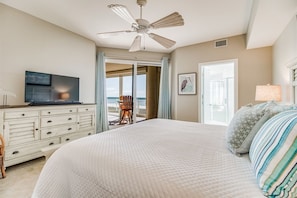 Een slaapkamer met een groot bed, een plafondventilator, een televisie op een dressoir en uitzicht op de oceaan door een schuifdeur.