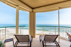 Un balcone coperto con due sedie e un tavolo, con vista su una spiaggia e una limpida visuale sull'oceano.