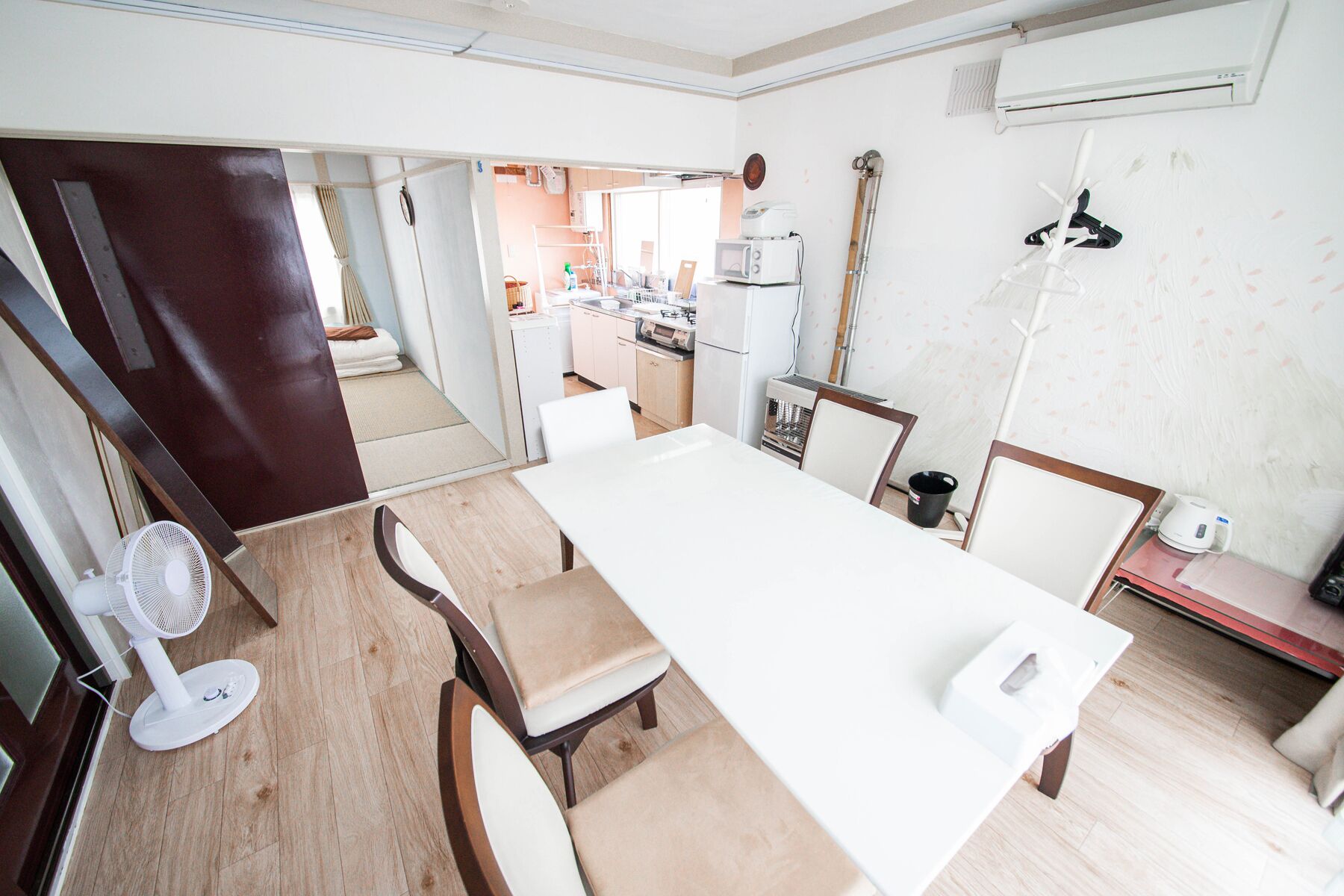 A modern kitchen with white appliances, a dining area with a long table and chairs, and a visible air conditioning unit on the wall.