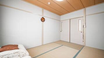 Une pièce avec un sol recouvert de tatamis, un lit avec une literie blanche et marron, un plafond en bois et une porte coulissante.