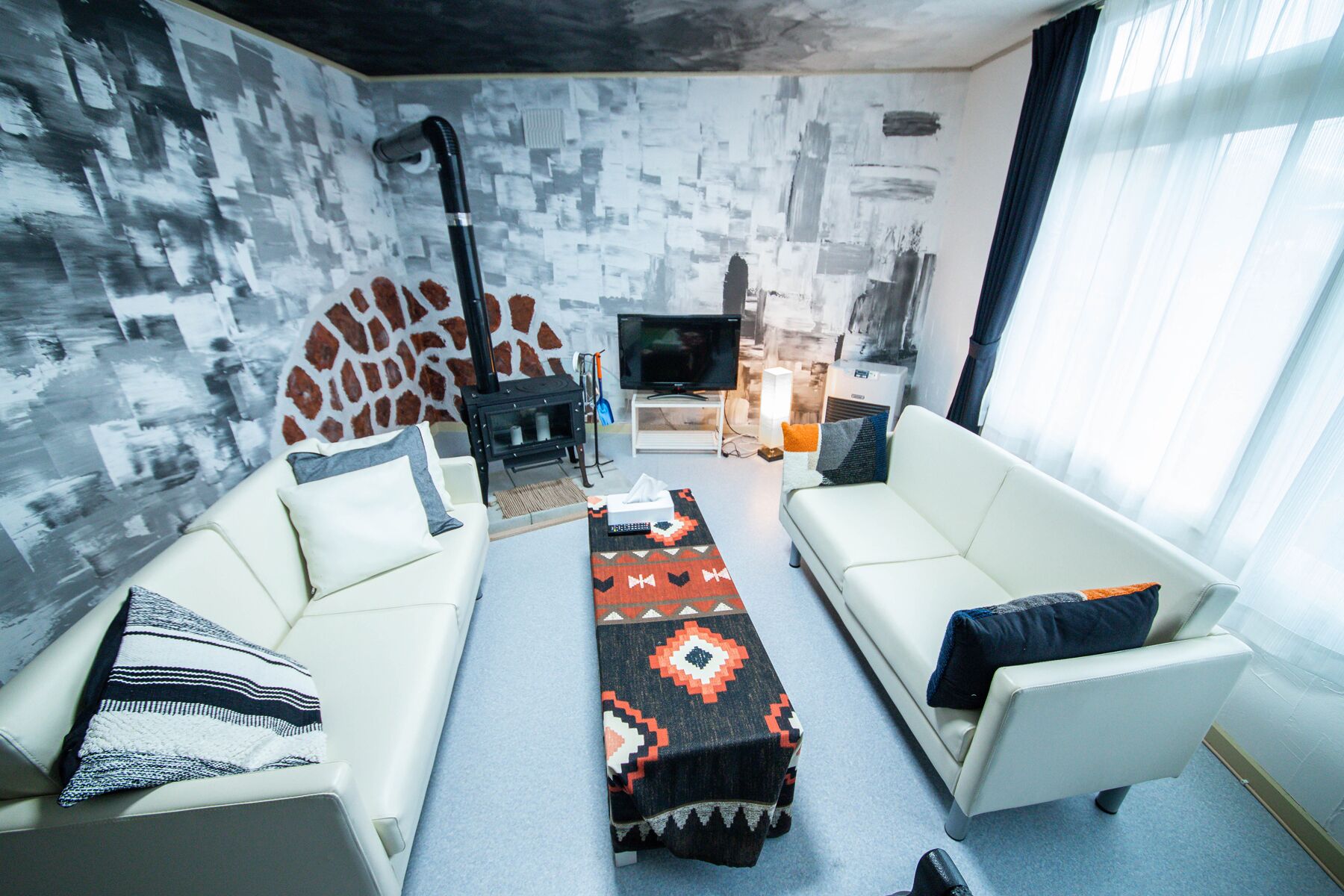 A modern living room with two white sofas, a patterned rug, a television, and a stone wall.