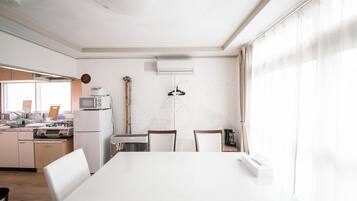 A modern kitchen with white appliances, a dining table, and a large window with sheer curtains.