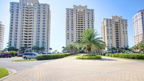 A multi-story residential building with a uniform facade, a paved walkway, and palm trees. - Beach Colony Tower 9C - Indoor Pool - HASSLE-FREE CHECK OUT (Perdido Key)