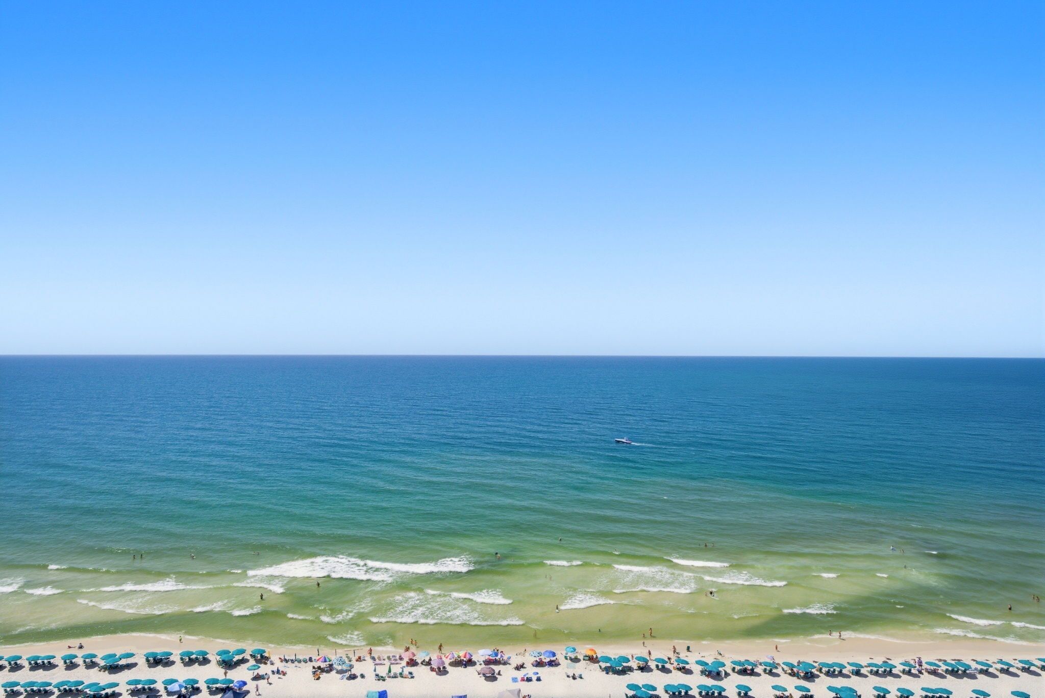 A beach with clear blue water, a sandy shore, and numerous umbrellas.