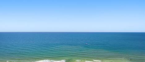 A beach with clear blue water, a sandy shore, and numerous umbrellas.