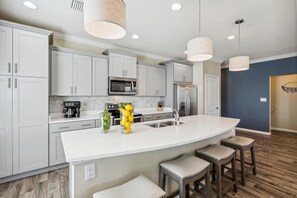 Una cocina moderna con armarios blancos, una isla grande con taburetes, electrodomésticos de acero inoxidable e iluminación colgante.