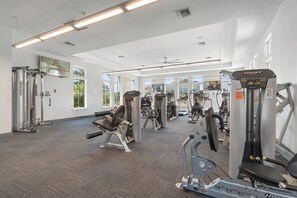 A gym with various exercise equipment, large windows, and a carpeted floor.
