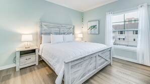 Un dormitorio con cama, mesitas de noche, ventilador de techo, ventana con persianas y vista a la ciudad.