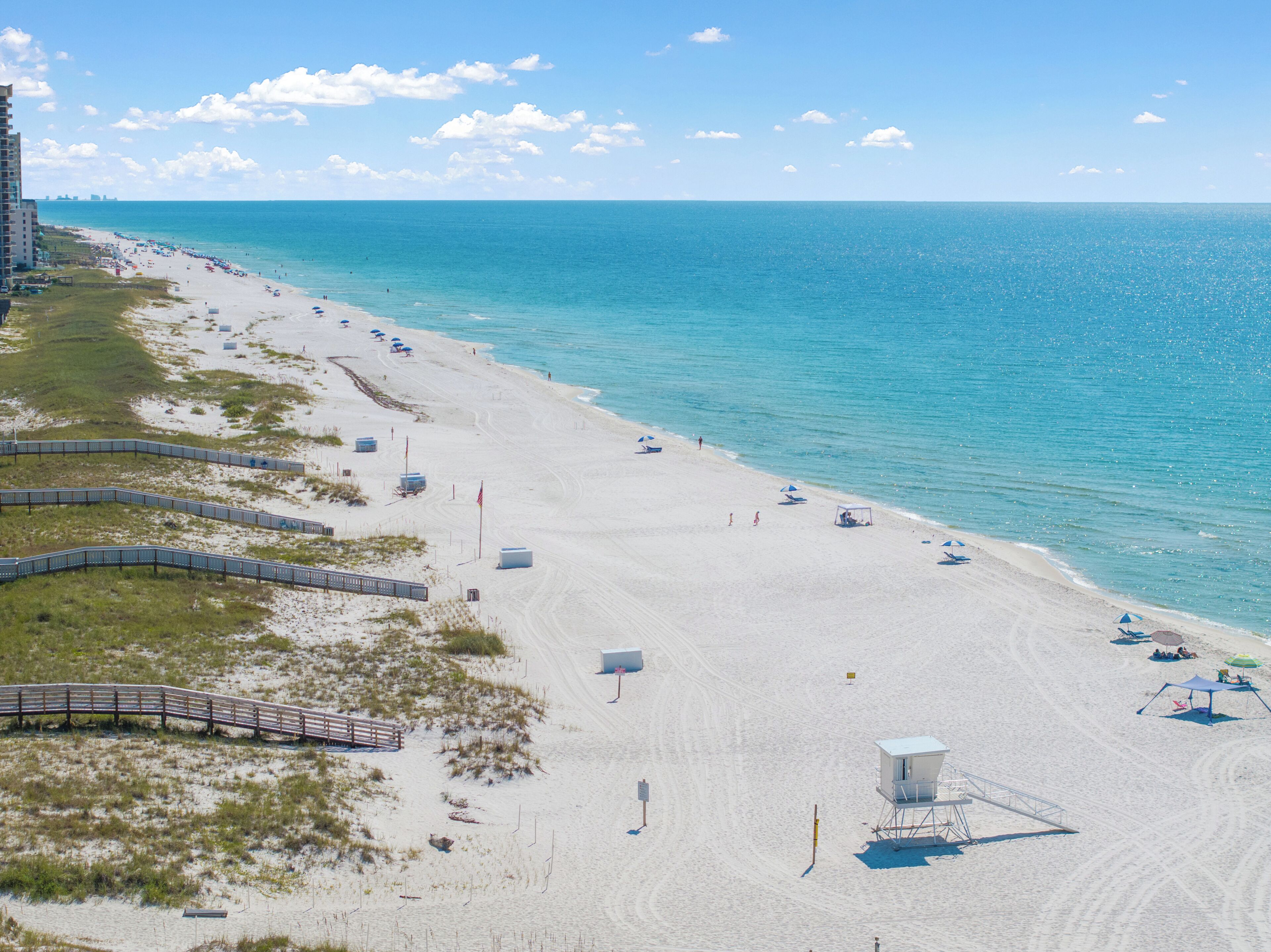 A beach with a lifeguard tower, a wooden boardwalk, and a clear view of the ocean.