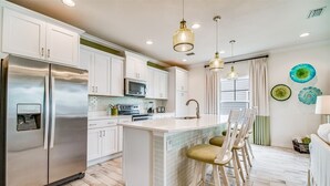 A modern kitchen with white cabinets, stainless steel appliances, a central island with bar stools, and pendant lighting. - Lost Key Villas Golf & Beach Club ~CS'ta on the Key -  NO HASSLE CHECK OUT (Pensacola)