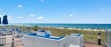 A deck with white wicker furniture and a view of the beach.