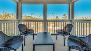 A covered outdoor seating area with a table and four chairs, overlooking a landscape with trees and buildings. - Escape at Lost Key Golf & Beach Club ~ Escape - NO HASSLE CHECK OUT (Pensacola)