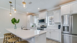 A modern kitchen with white cabinetry, stainless steel appliances, a central island with stools, and pendant lighting. - Escape at Lost Key Golf & Beach Club ~ Escape - NO HASSLE CHECK OUT (Pensacola)