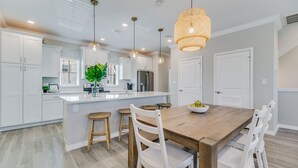 A modern kitchen with white cabinetry, a central island with stools, pendant lighting, and a dining table with chairs. - Escape at Lost Key Golf & Beach Club ~ Escape - NO HASSLE CHECK OUT (Pensacola)