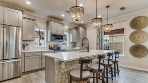 A modern kitchen with stainless steel appliances, a large island with bar stools, and decorative wall plates. - Lost Key Townhomes 14274 ~ Flip Flop Stop  -  NO HASSLE CHECK OUT (Pensacola)