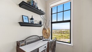 Ein Zimmer mit Esstisch, Korbstühlen, Blick ins Freie durch ein großes Fenster sowie Regalen mit Büchern und Dekoration.